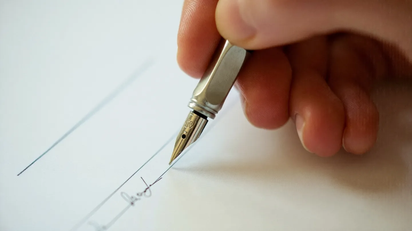 Macro close-up of a hand signing a document with a fountain pen, the nib touching the signature line